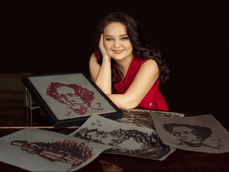 Die Pianistin Markovina in rotem Kleid am Flügel, auf dem gezeichnete Portrais von Komponisten liegen