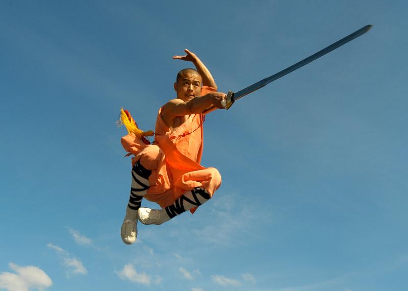 Shaolin Mönch in orangener Kutte springt in der Luft