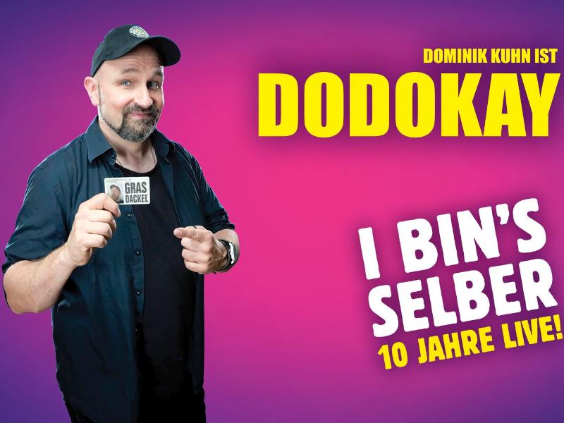 Dodokay steht vor pink-violettem Hintergrund und hält einen weißen Ausweis mit der Aufschrift Grasdackel in der Hand. Rechts im Eck steht "Dodokay" und unten rechts "ich bin's selber-10 Jahre"